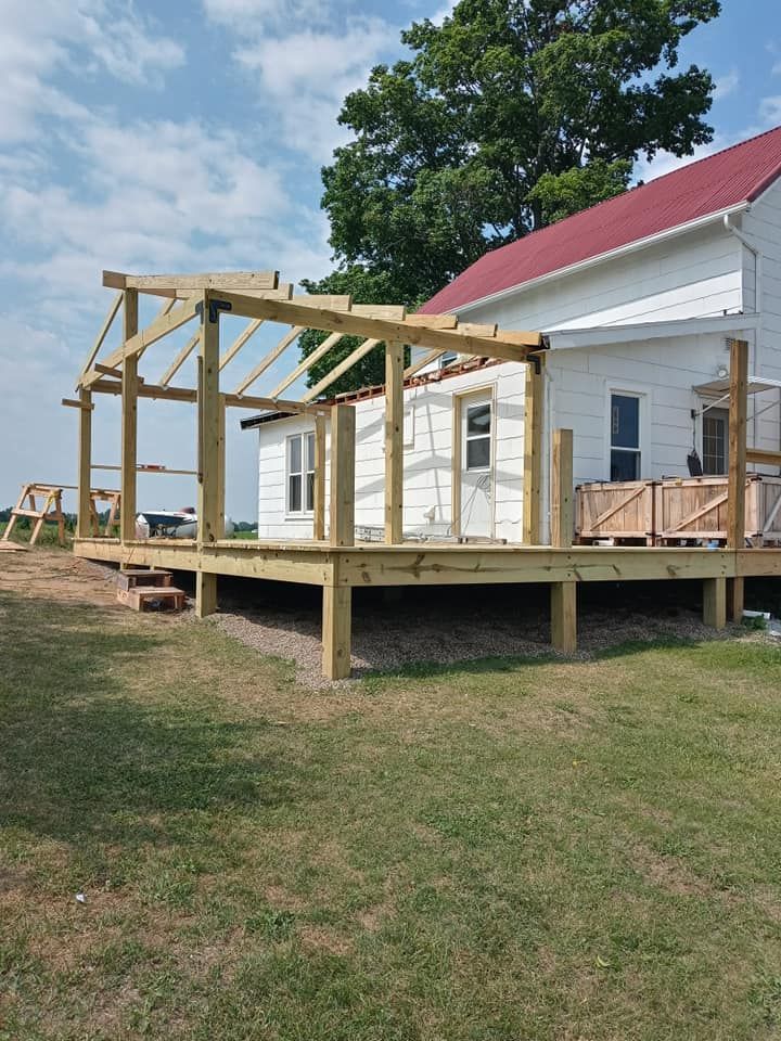 Wooden deck and pergola under construction next to a white house with a red roof.