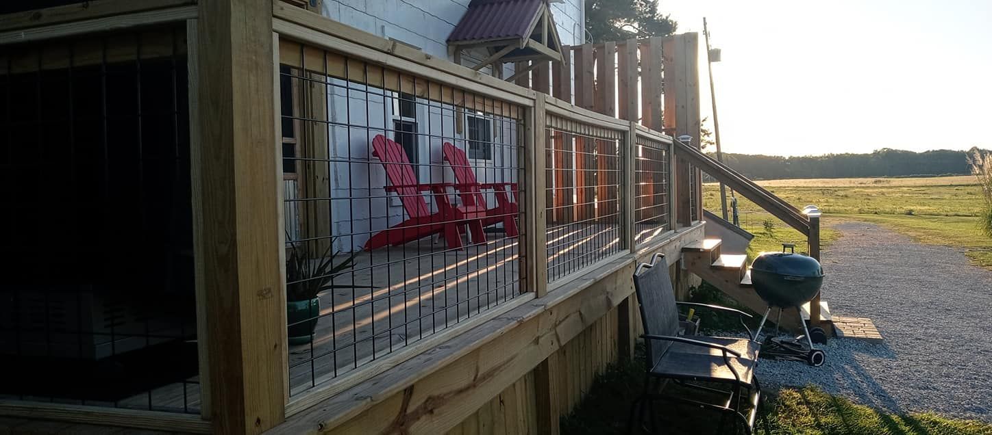A wooden deck with red chairs, a grill, and a grassy field in the background.