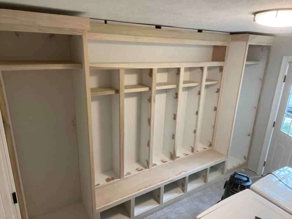 Built-in white wooden entryway storage unit with shelves, hooks, and bench.