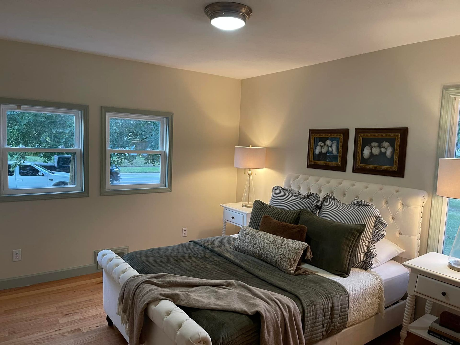 Bedroom with bed, nightstands, windows, art, and neutral-toned walls.