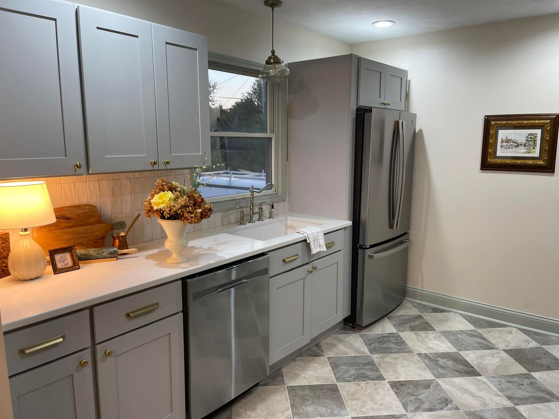 Gray kitchen cabinets and appliances with a white countertop and checkered floor.