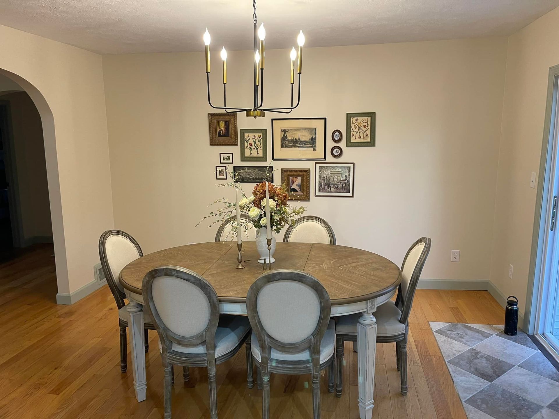 Dining room with round table, six chairs, gallery wall, chandelier, and hardwood floors.