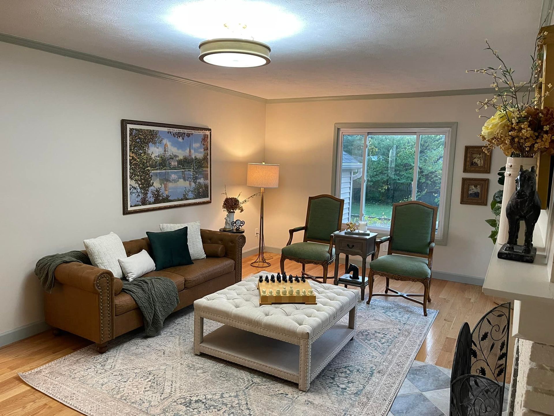 Living room with brown leather sofa, green chairs, and a tufted ottoman on a patterned rug.