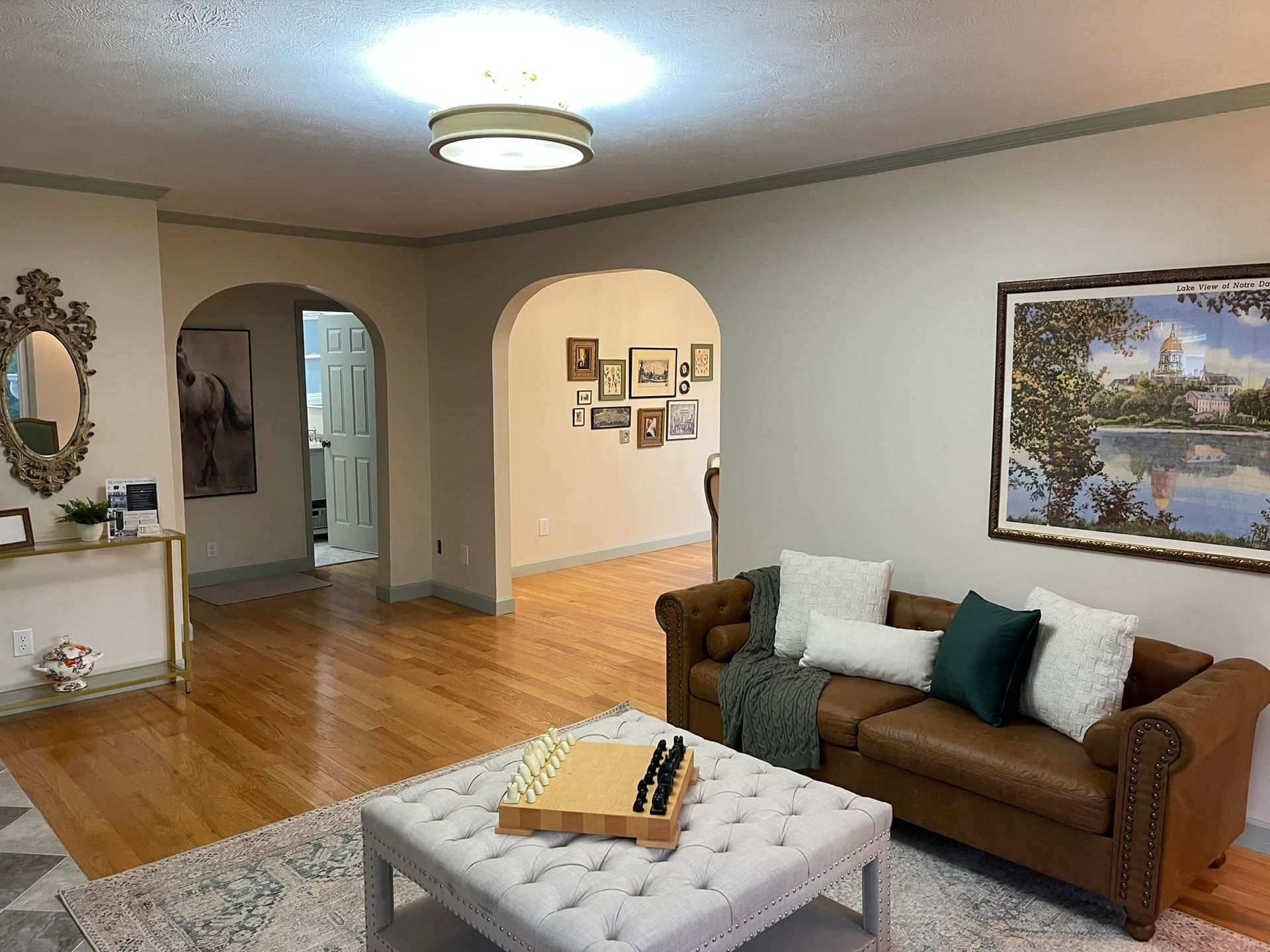 Living room with brown leather sofa, archways, wooden floors, and a light-colored ceiling.