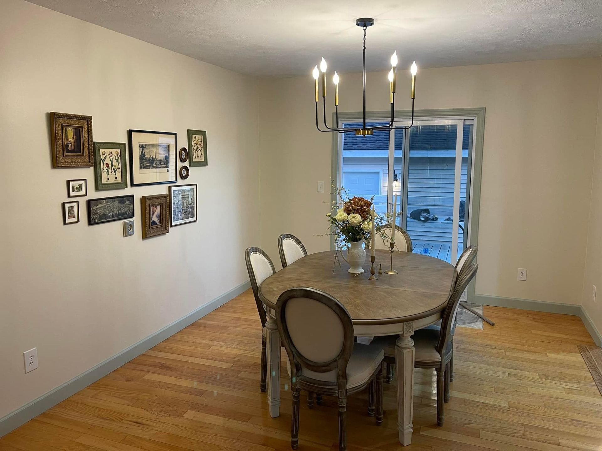 Dining room with a table, chairs, artwork on the wall, and a chandelier. A sliding glass door leads outside.