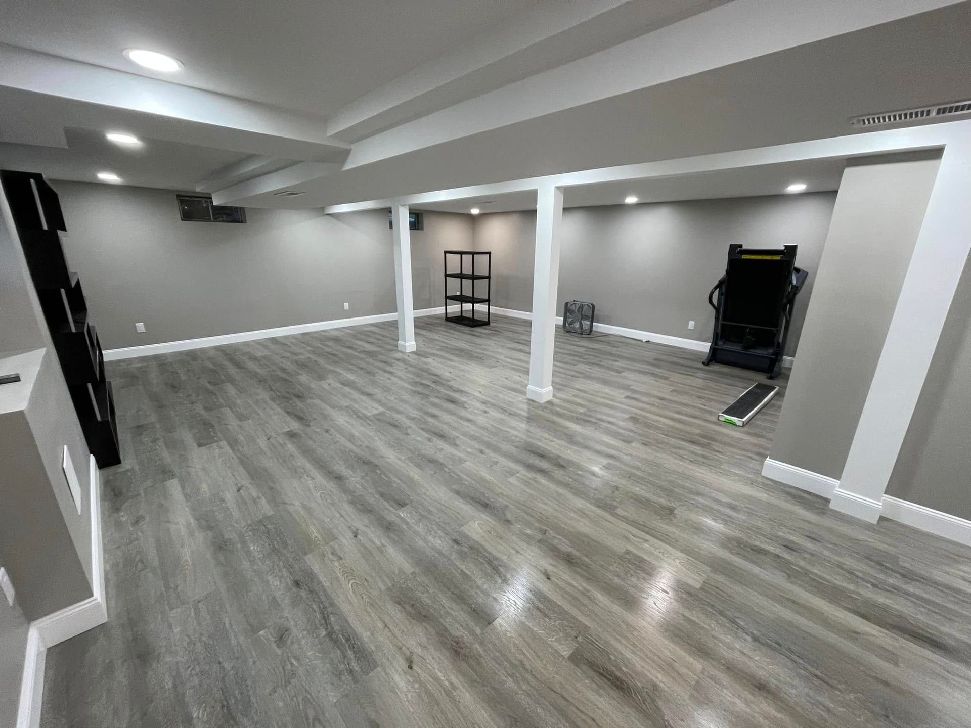 Spacious basement with gray flooring, white support beams, and a treadmill.