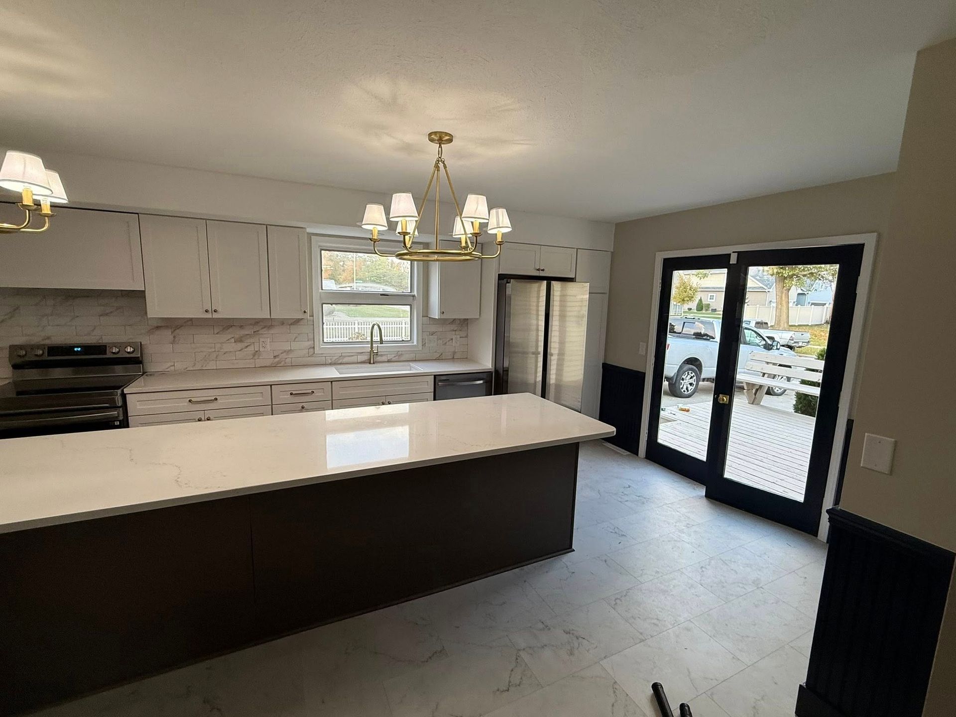 Modern kitchen with white cabinets, dark island, and glass doors.