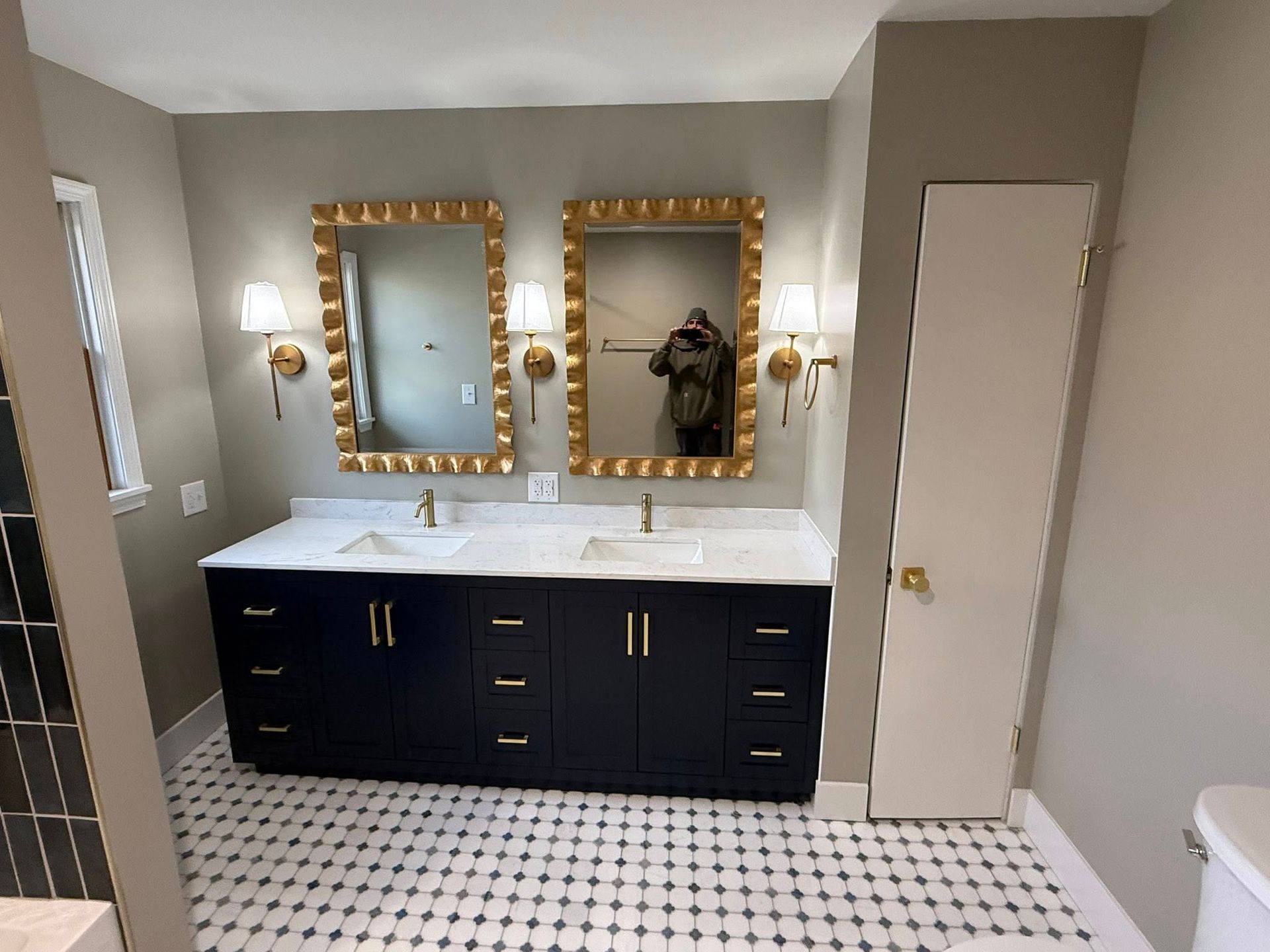 Bathroom with navy vanity, gold mirrors, white countertops, and patterned floor.