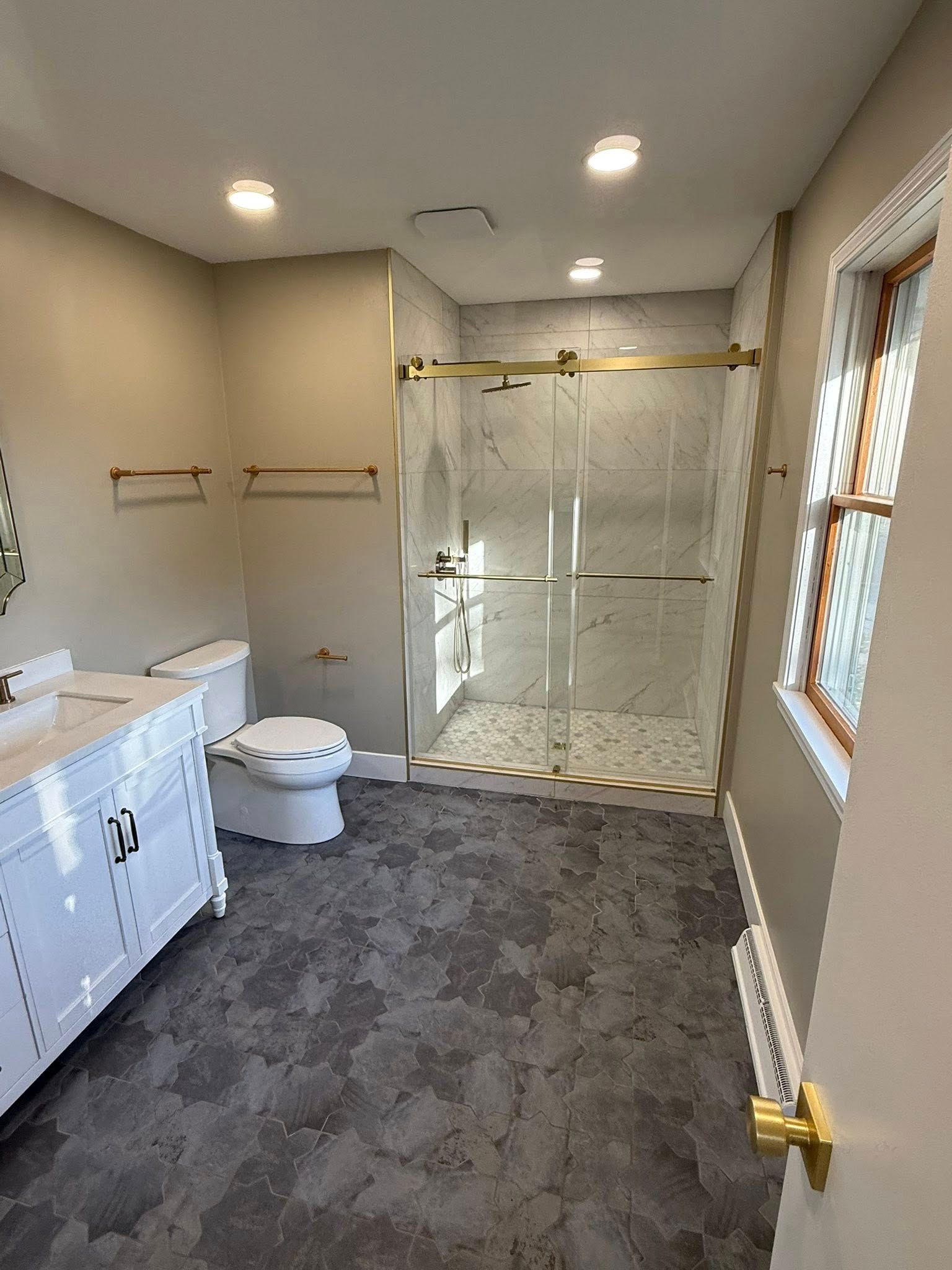 Bathroom with white vanity, toilet, and shower with gold trim; gray tiled floor.