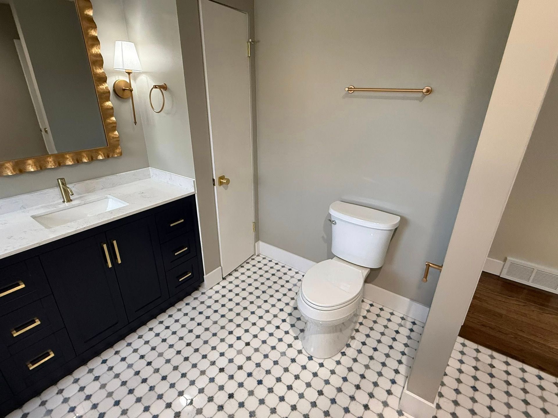 Bathroom with navy vanity, gold mirror frame, white toilet, patterned floor, and gold towel bar.