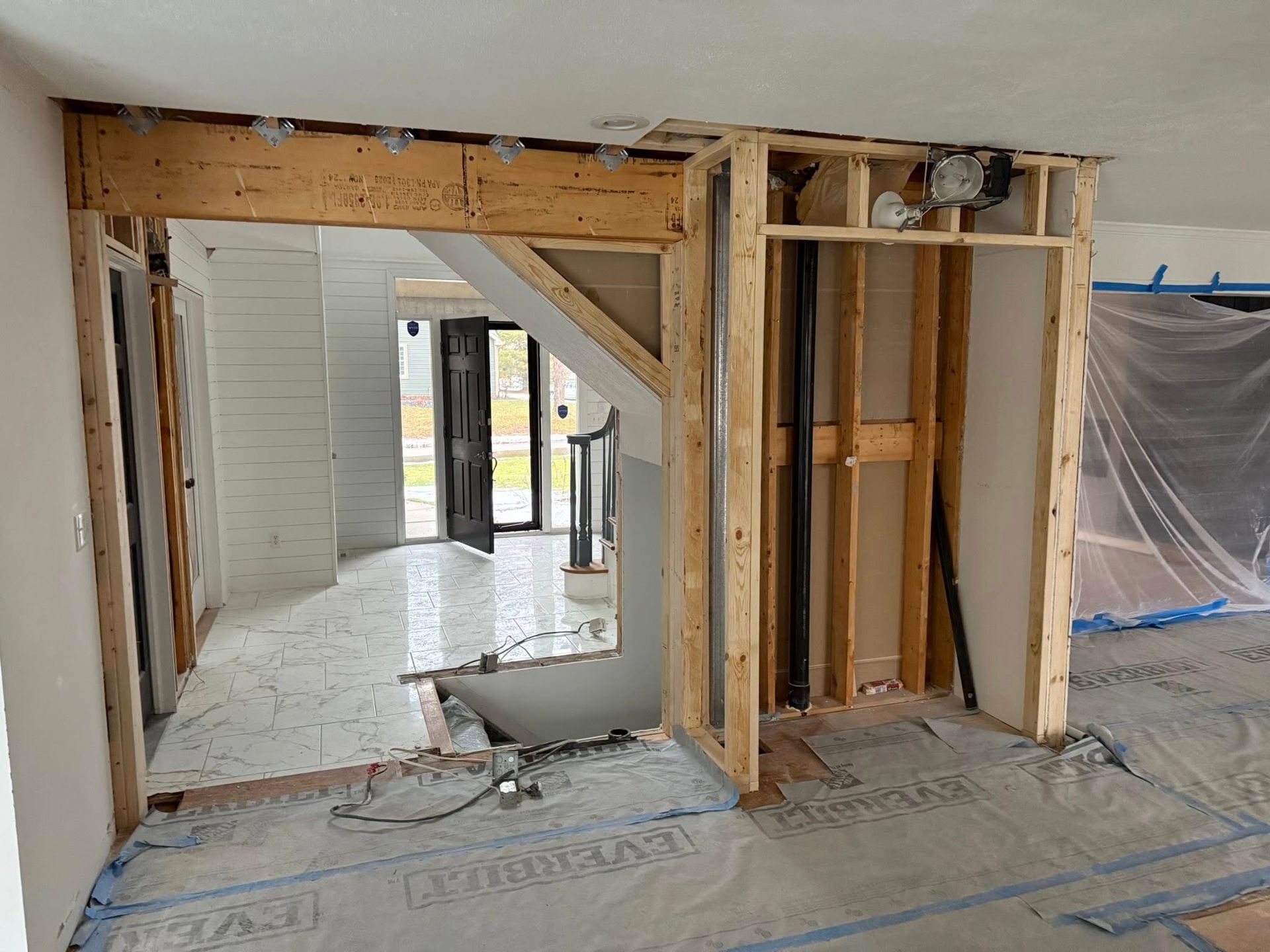 Interior under construction: framed doorways, support beam, visible plumbing, plastic sheeting covering floors.