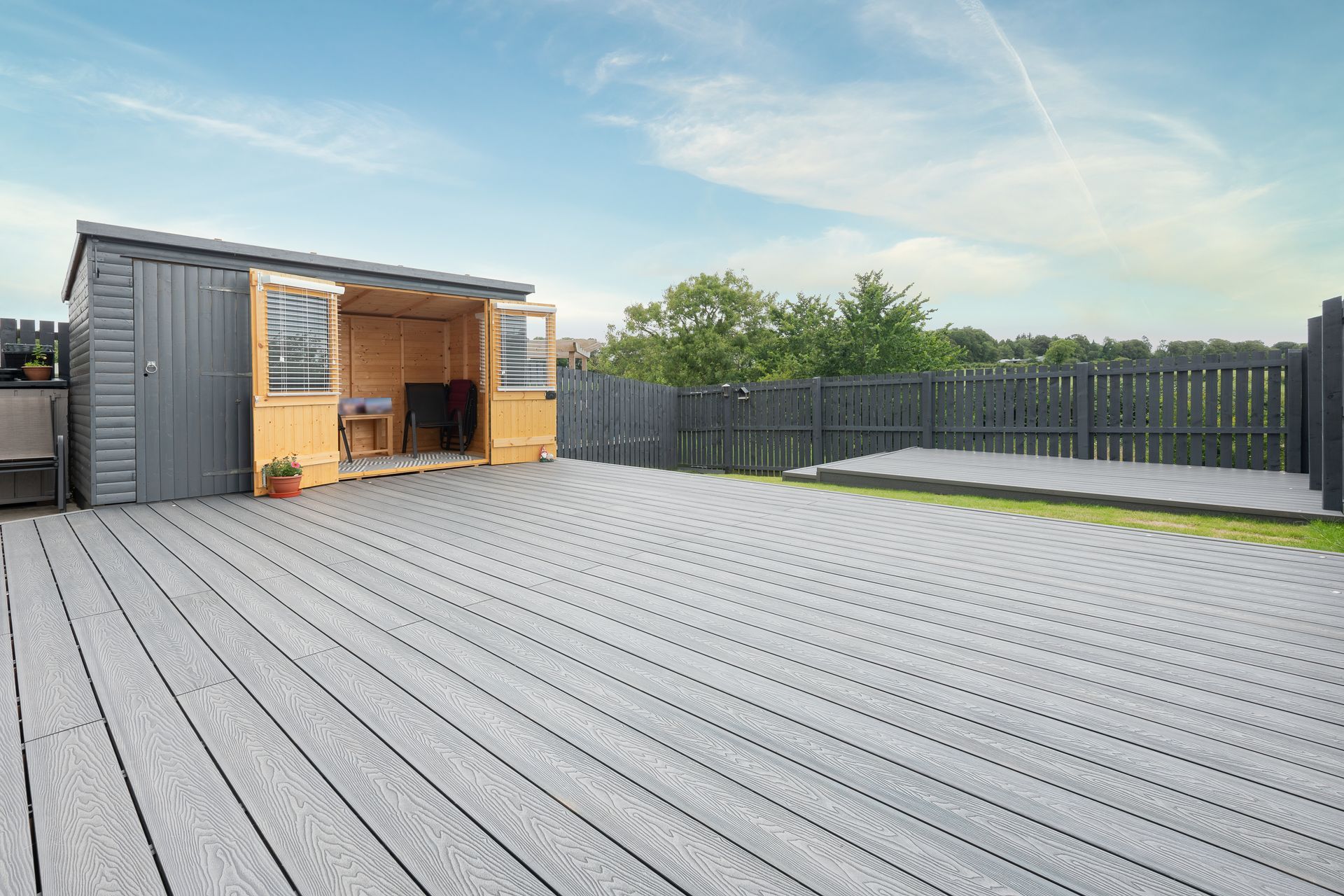 Gray wooden deck with shed, fenced yard, and blue sky.
