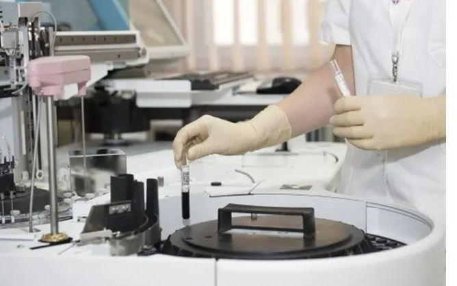 Trabajador de laboratorio con guantes sosteniendo un tubo de ensayo cerca del equipo de laboratorio.