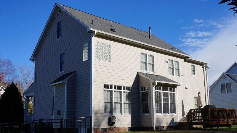 Beige two-story house with gray roof, sunroom, and wooden deck under a blue sky.