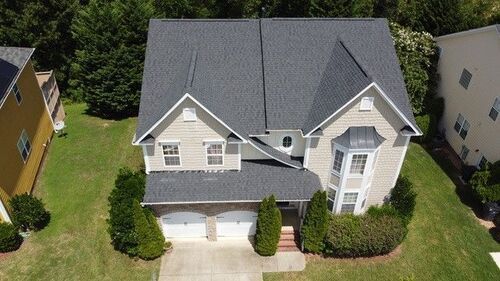 Two-story house with gray roof and beige siding, two-car garage, and manicured lawn.