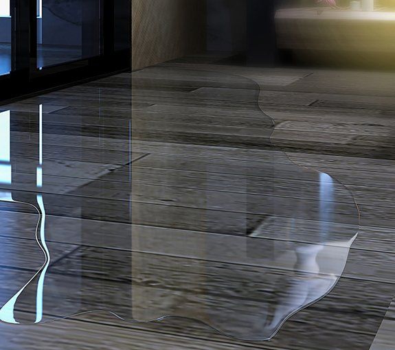 Water spilled on a wooden floor. Reflective surface shows light.