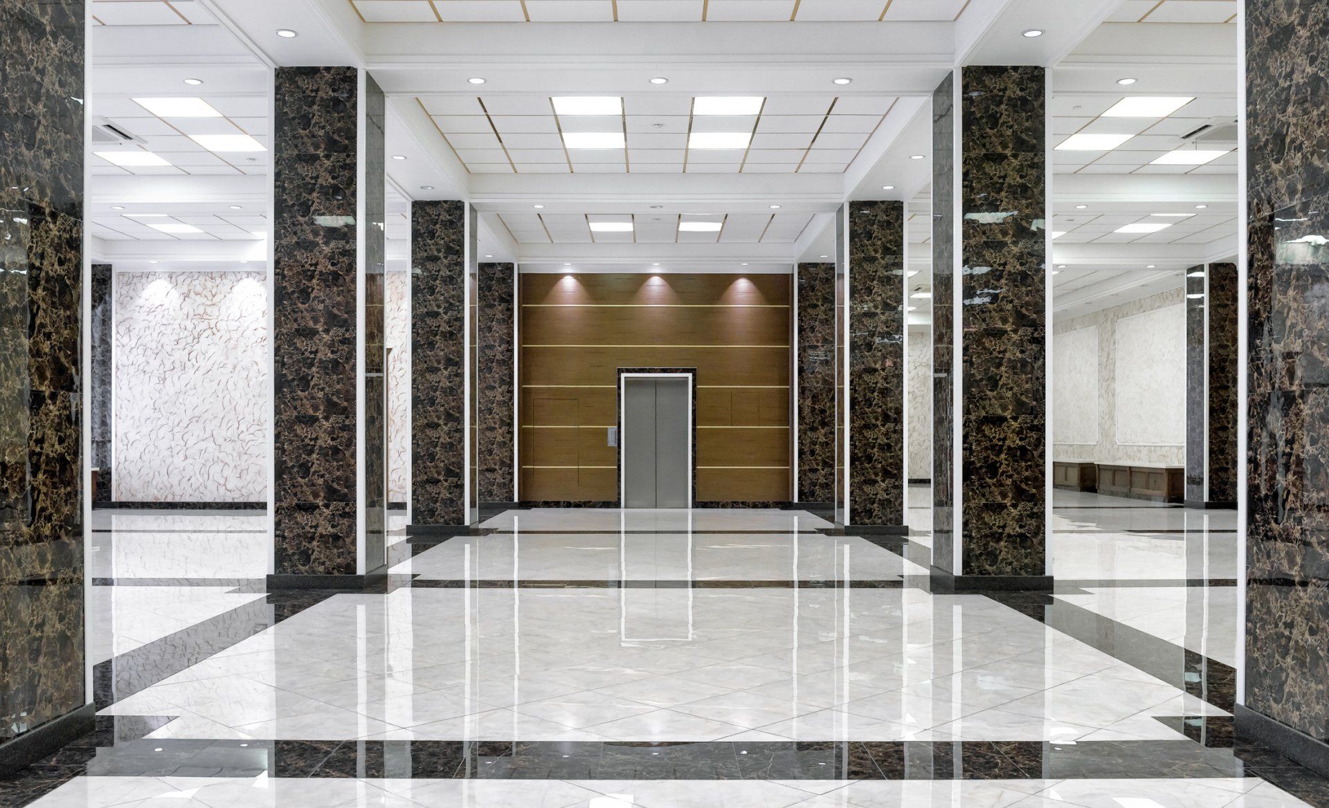 Interior lobby with marble floor and columns, elevator centered on back wall.