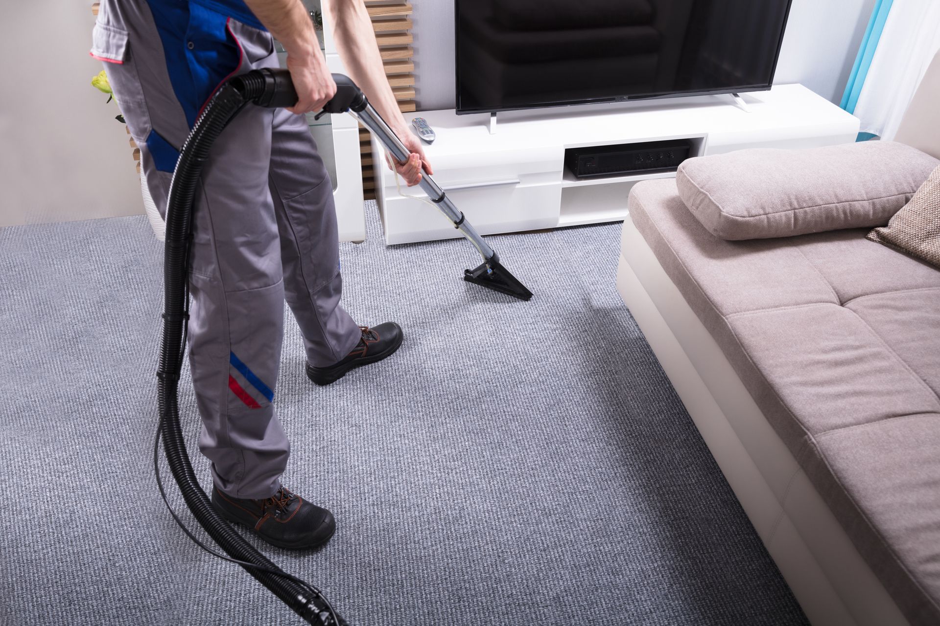 Close-up of worker using a vacuum cleaner to perform residential carpet cleaning in a living room.