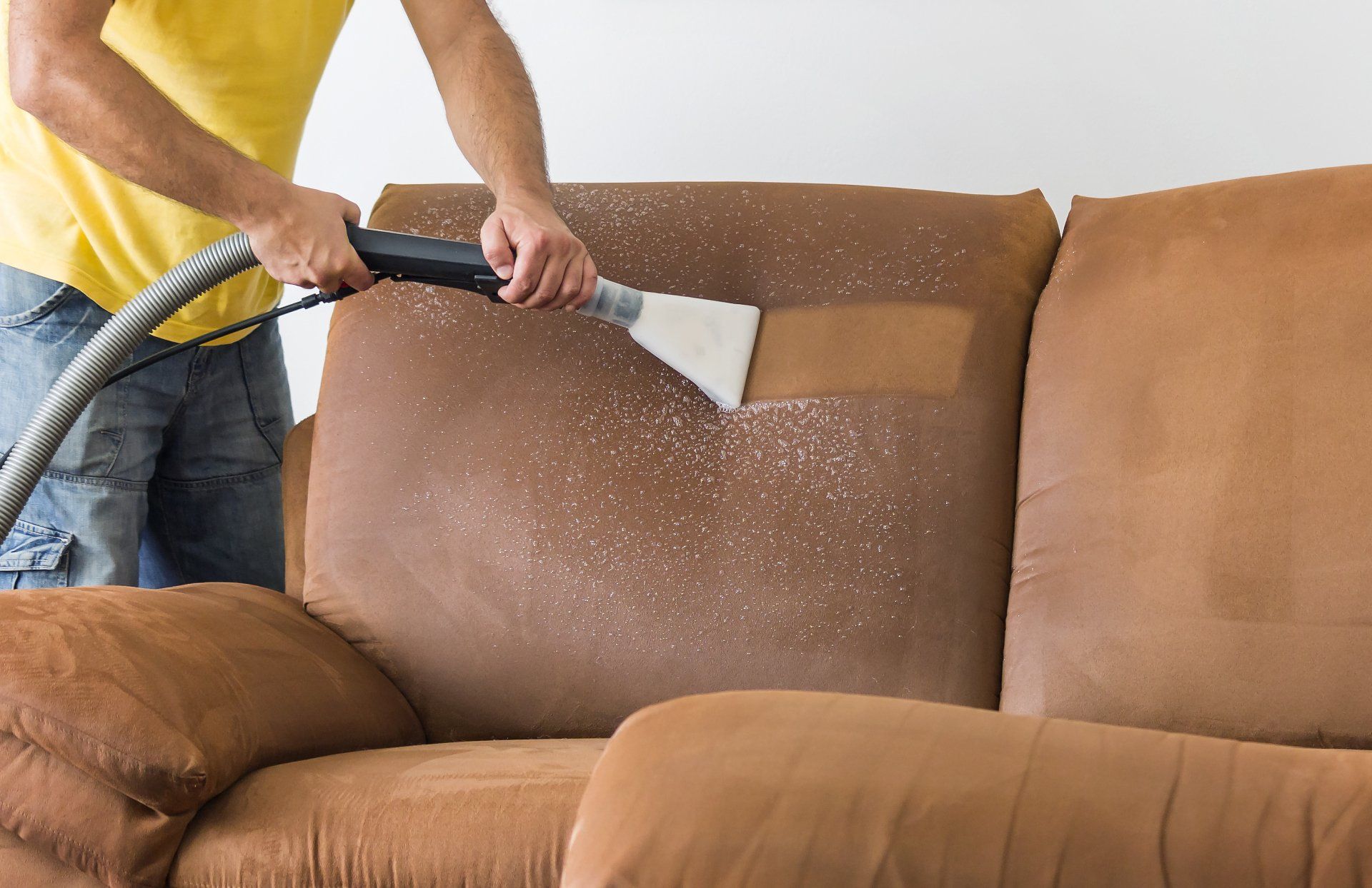Person cleaning a brown couch cushion with a carpet cleaner, creating a light-colored stripe.