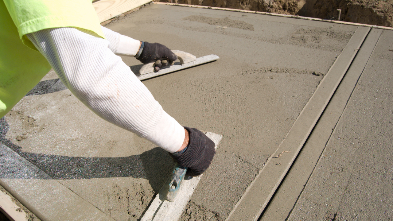 A person smoothing a concrete slab with handheld flat tools