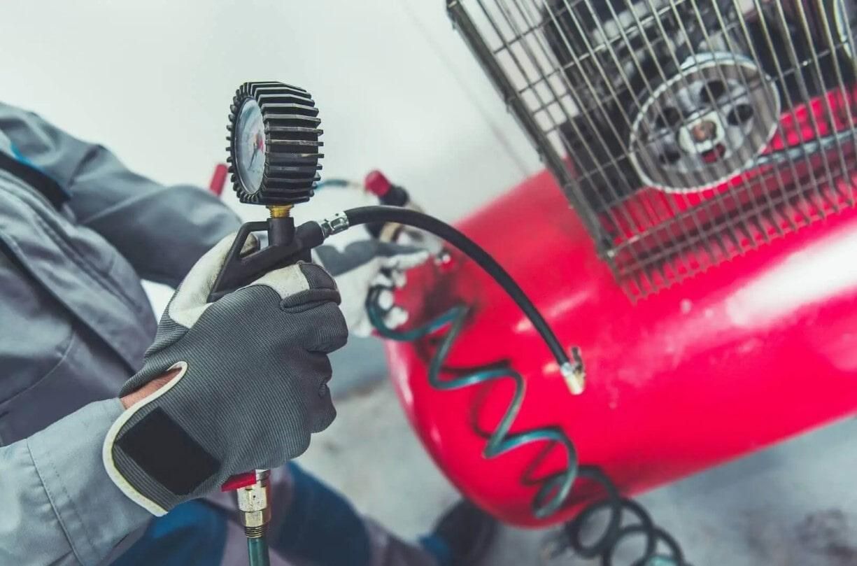 Un hombre sostiene un medidor al lado de un compresor de aire.