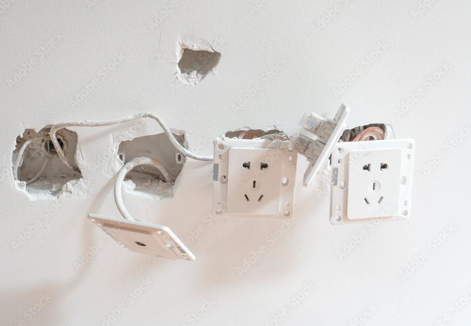 Electrical outlet with burn marks and exposed wiring on a beige wall.