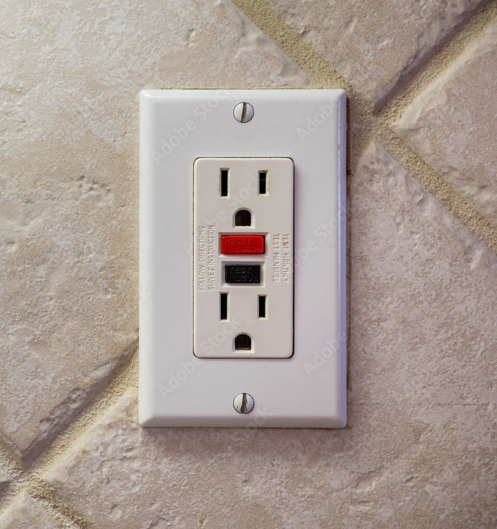 White GFCI electrical outlet with red reset button on a textured wall.