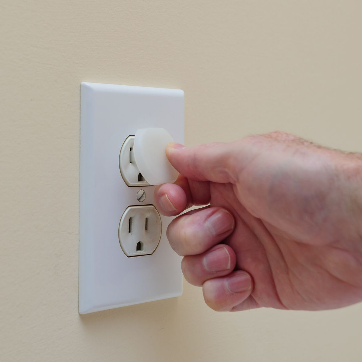 Hand inserting a white outlet cover into an electrical outlet. Beige wall. Hand inserting a white outlet cover into an electrical outlet. Beige wall.