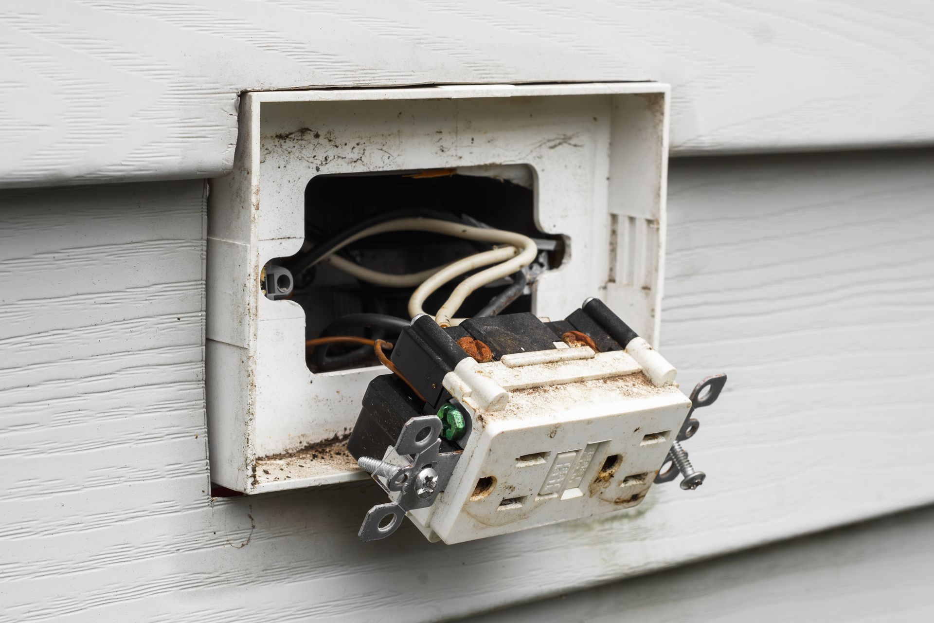 Damaged outdoor electrical outlet with exposed wires, mounted on white siding.