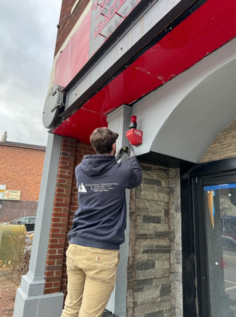 Electrical outlet with burn marks and exposed wiring on a beige wall.