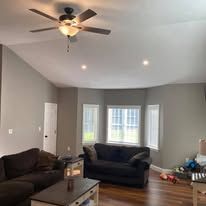 Person installing or repairing a black ceiling fan on a white ceiling.
