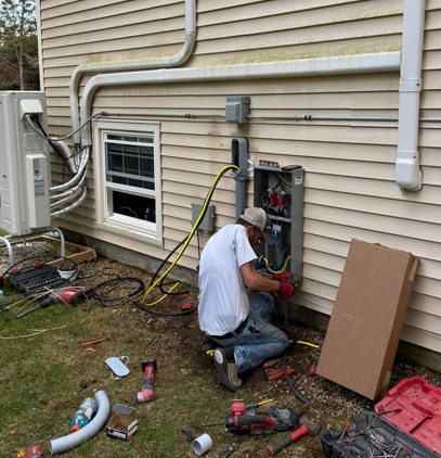 Hand testing an electrical outlet with red and black probes. Wires are visible, wall is white.
