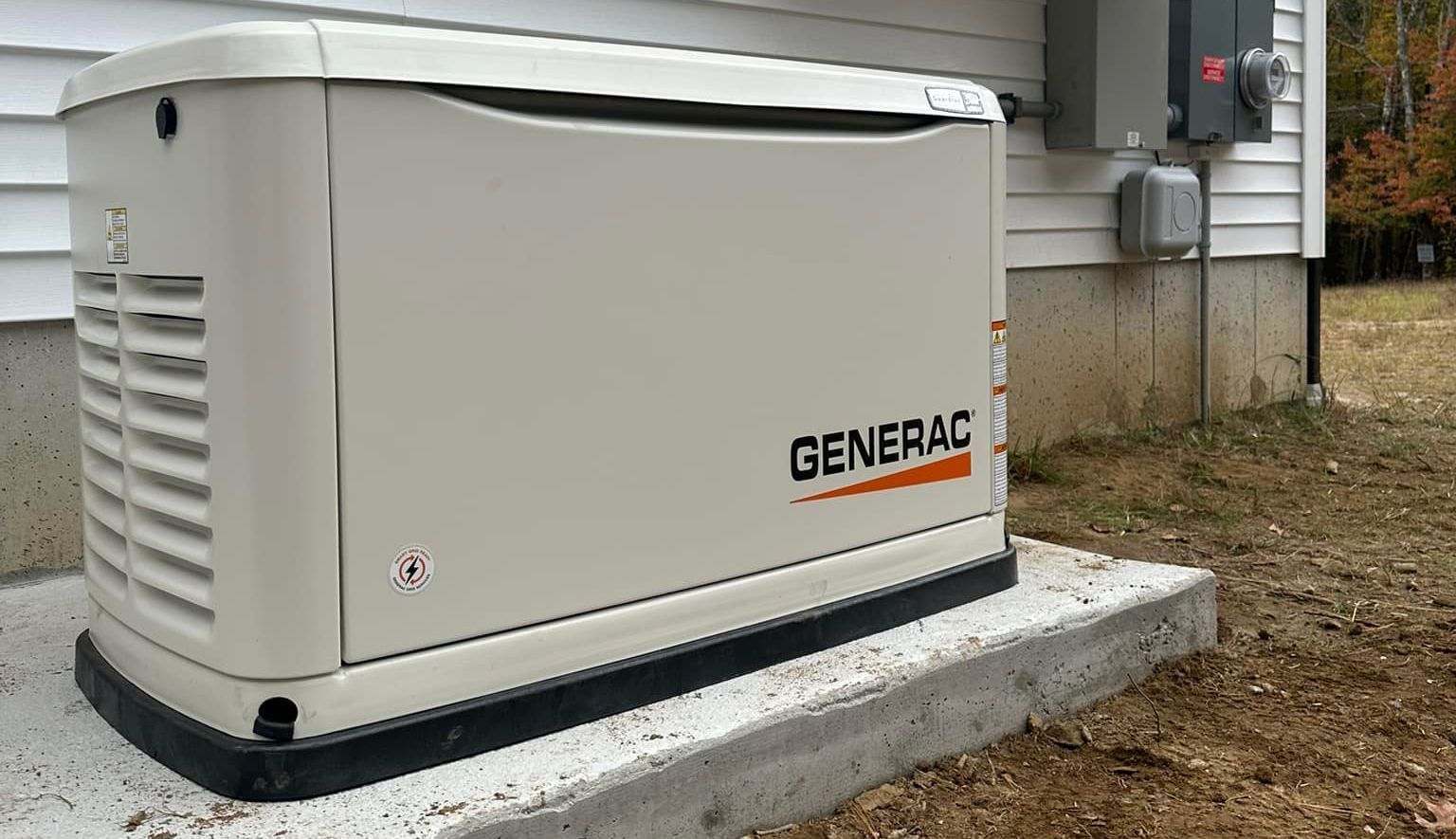 Generator next to a house with gravel border on grass under a cloudy sky.