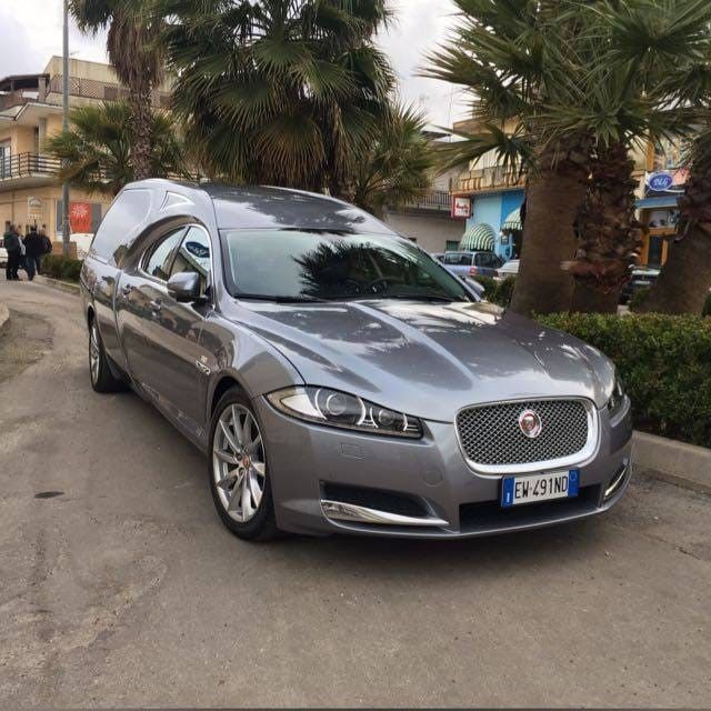Moderna casa bianca con tetto spiovente, prato e un'auto parcheggiata davanti.
