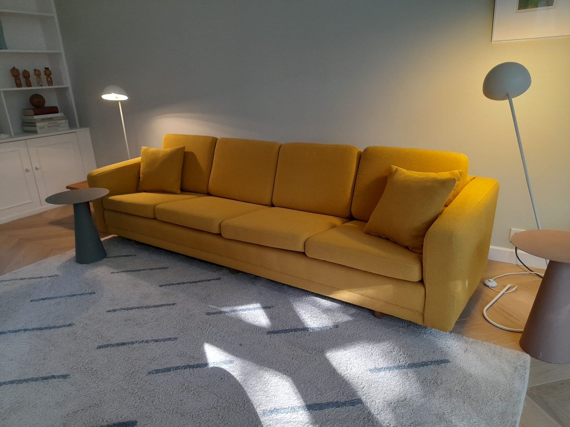 Gele bank in een kamer met een kleed, nachtkastjes en staande lampen.