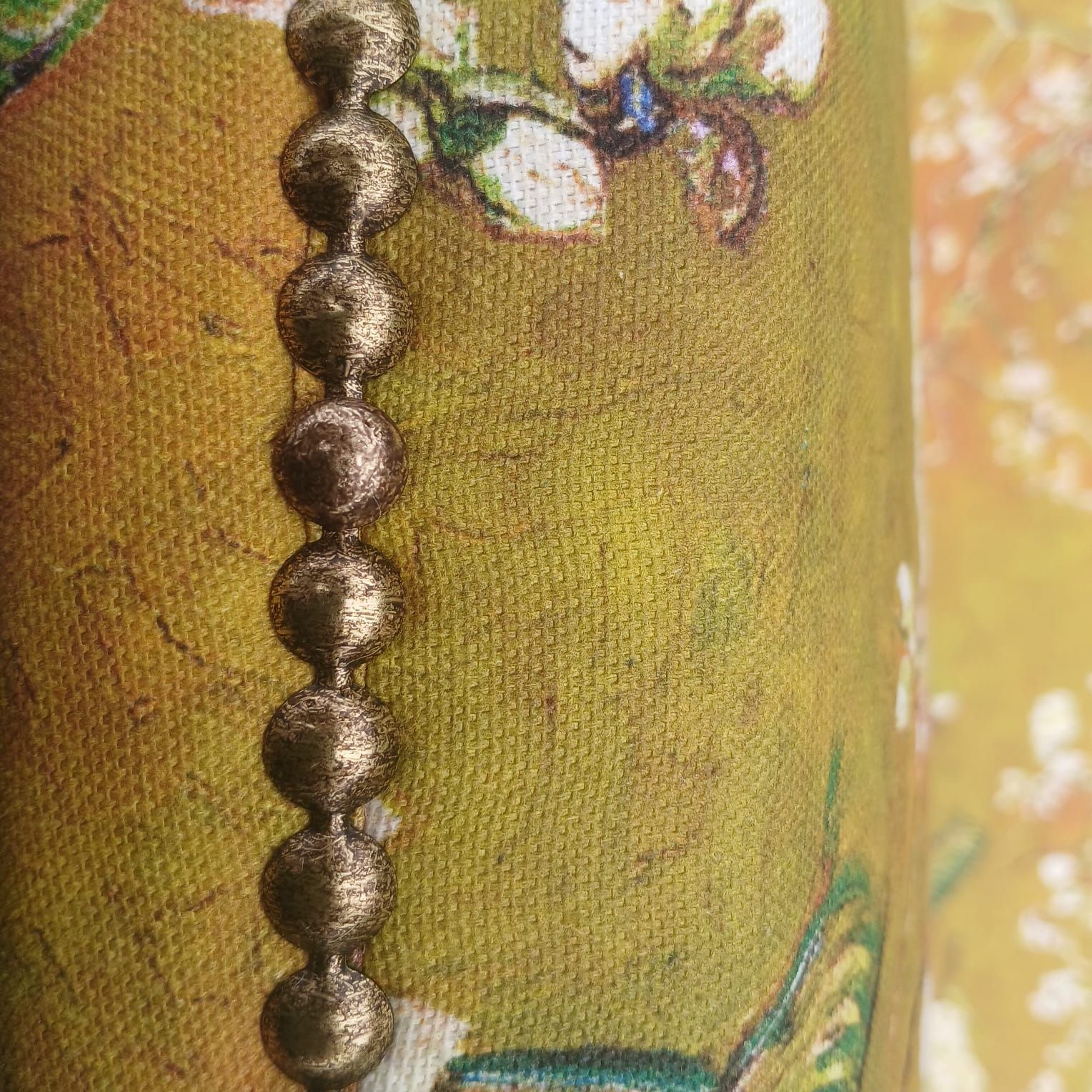 Een rij bruine, metalen kralen op een stof met een patroon in geel- en groentinten.