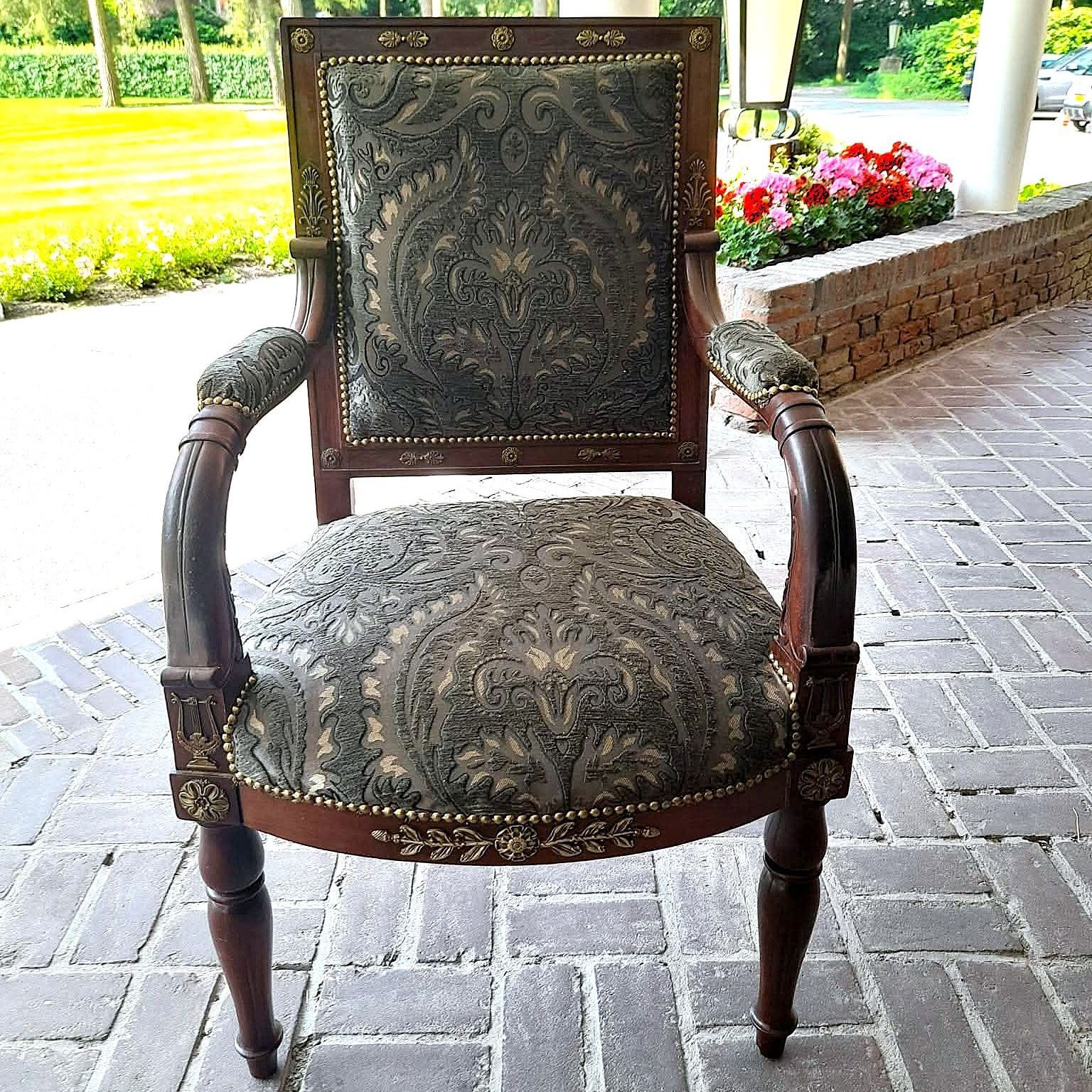 Een sierlijke antieke fauteuil met een donkerhouten frame en gebloemde groene bekleding staat op een stenen terras.