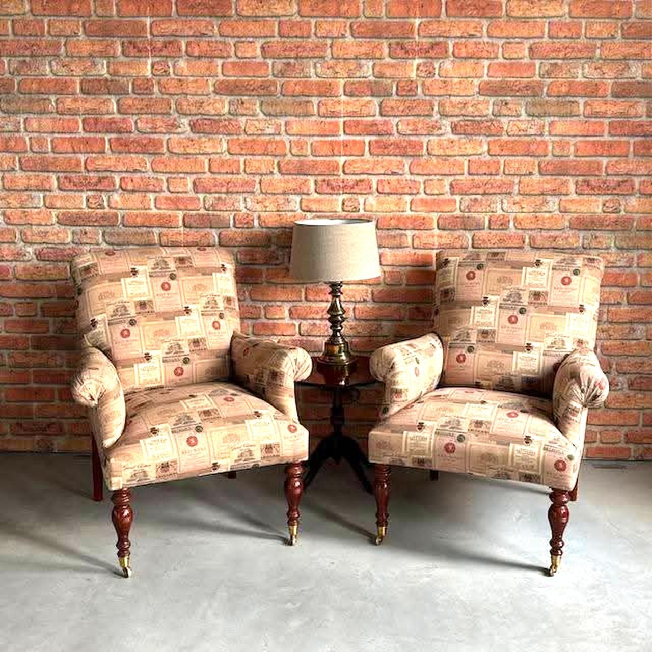 Twee fauteuils met patroon staan naast een klein tafeltje met een lamp tegen een bakstenen muur.
