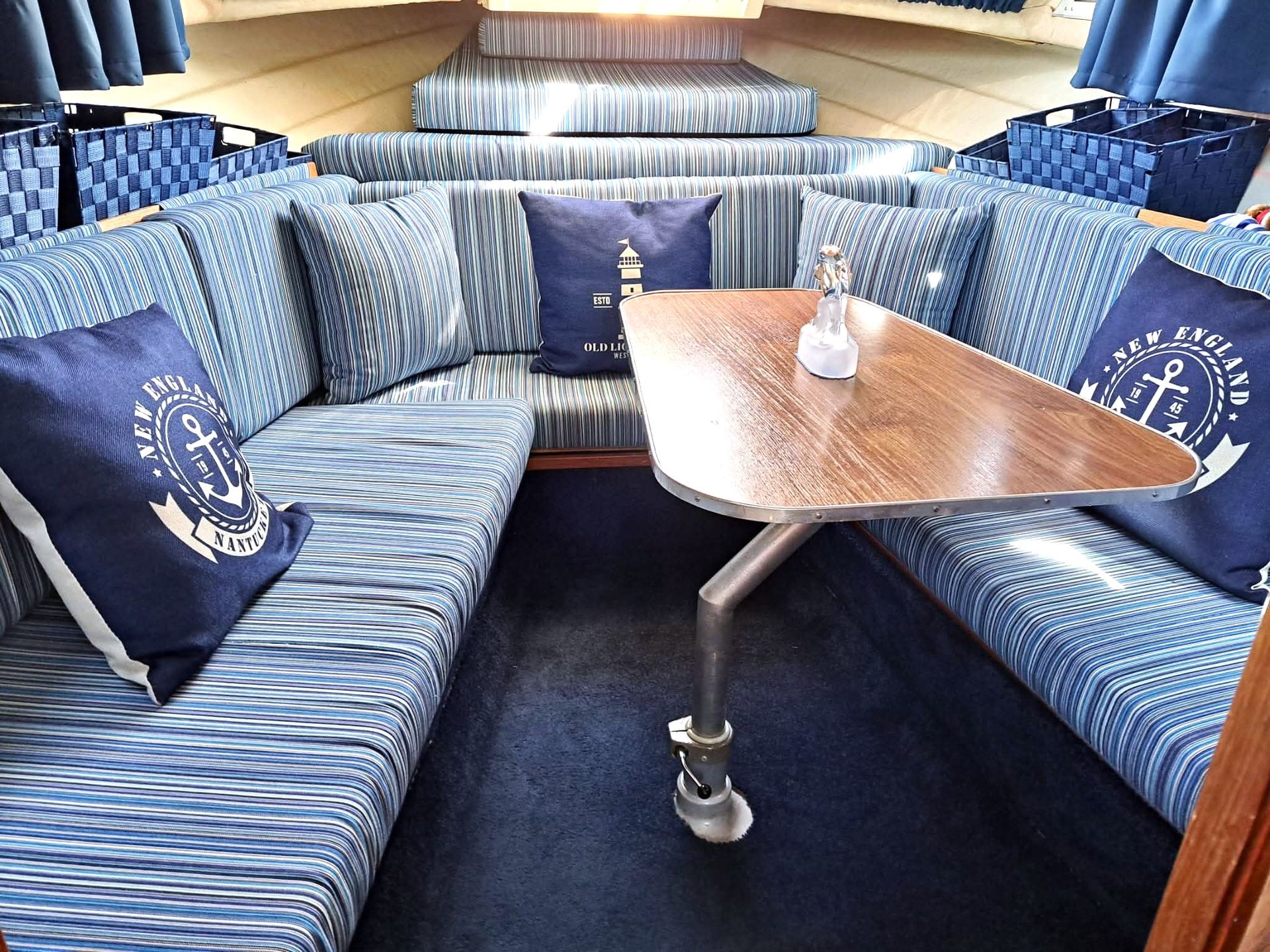 Gezellig interieur van een boothut met blauw-witte bekleding, donkerblauw tapijt en een klein houten tafeltje.