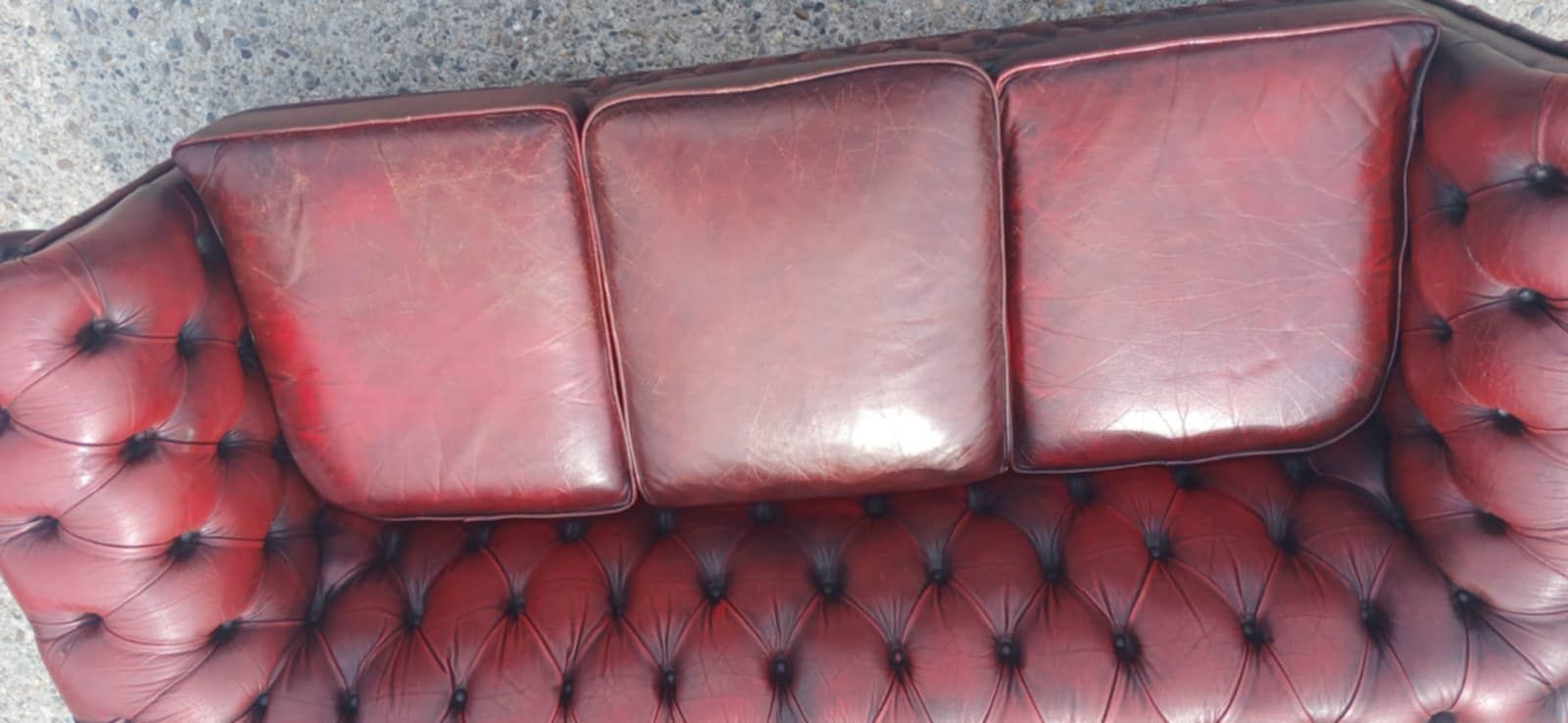 Een rode leren Chesterfield-bank met drie kussens en knoopjes, van bovenaf gezien.