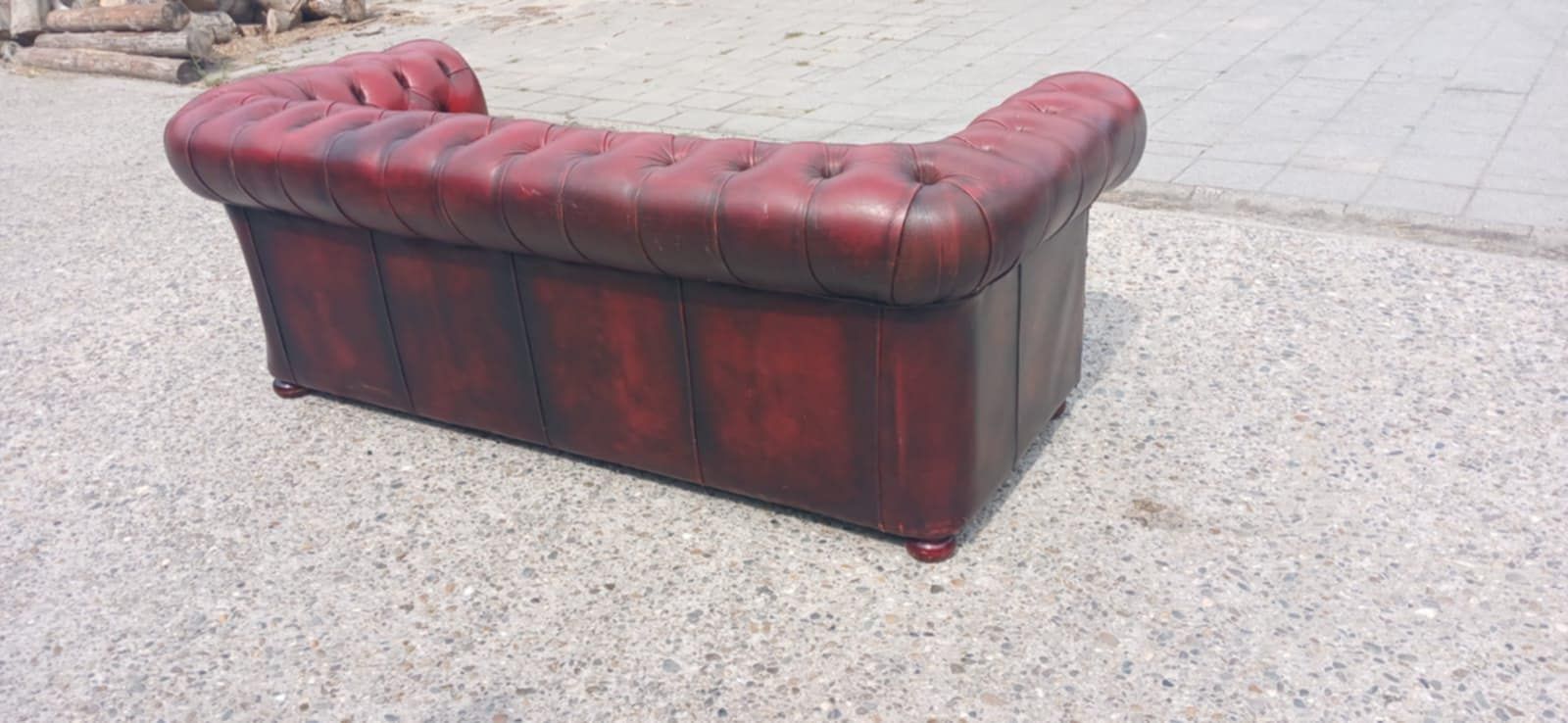 Een rode leren Chesterfield-bank staat op een grijs, gespikkeld oppervlak.