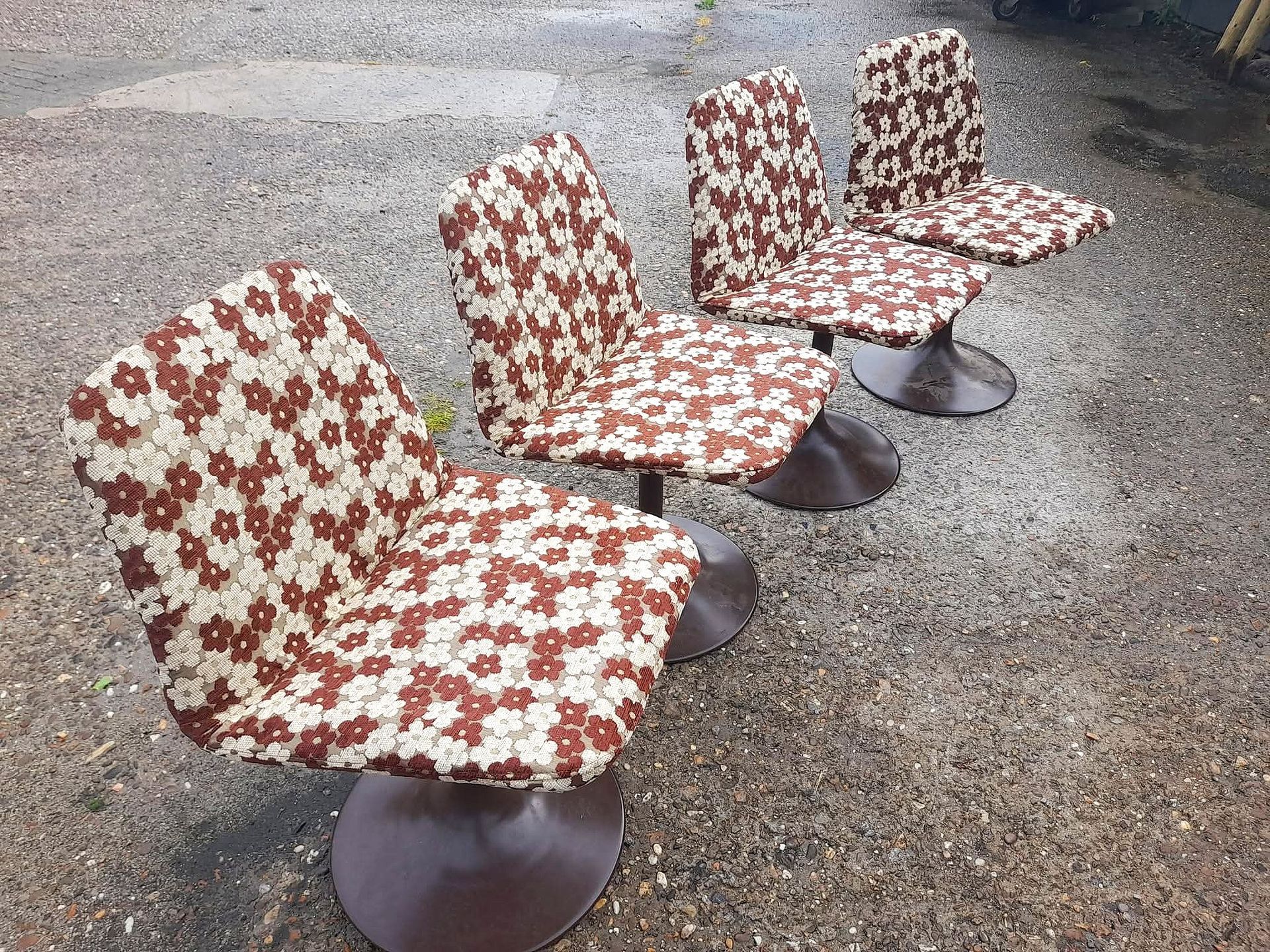 Vier vintage draaistoelen met bekleding met bruin en wit bloemenpatroon, op een grindvloer.