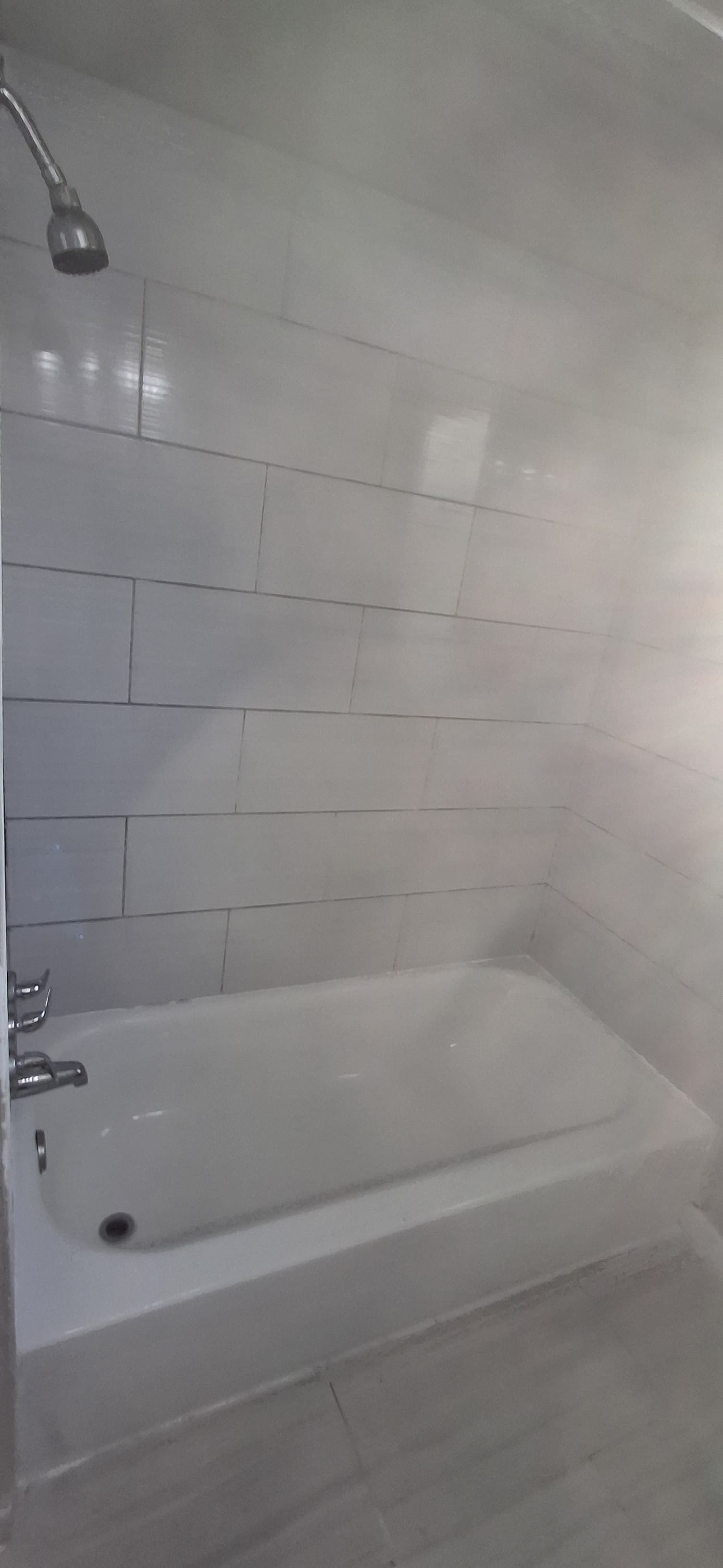 A white tiled shower with a bathtub, a showerhead, and silver fixtures.