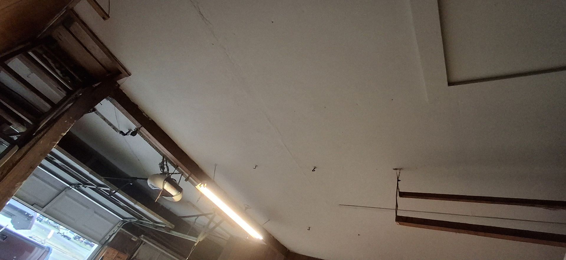 A white ceiling with a long fluorescent light and wooden beams.