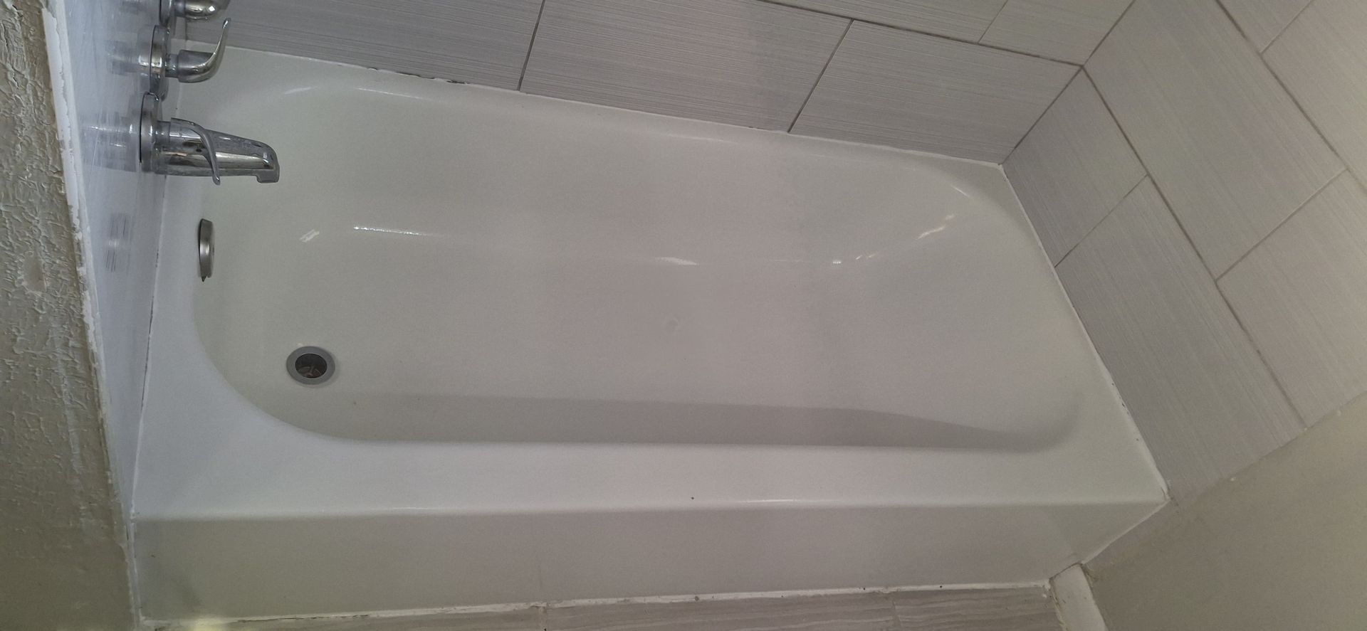 White bathtub in a tiled bathroom with silver faucet and drain.