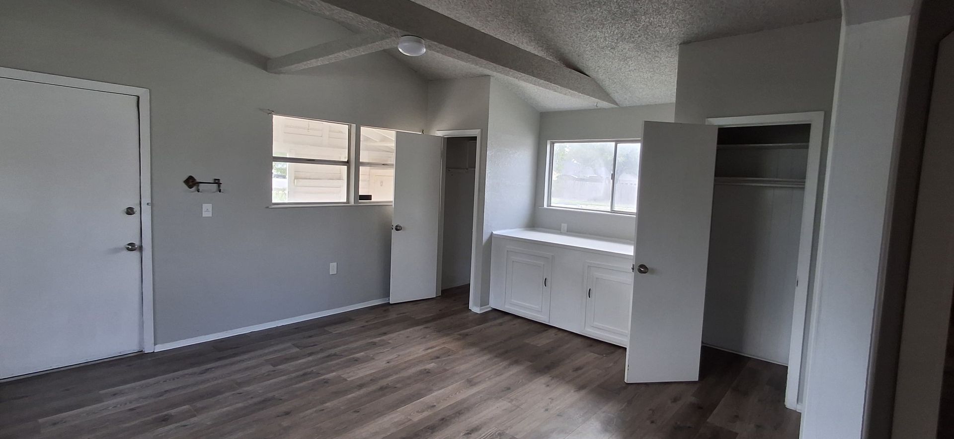 Interior view of a room with gray walls, wooden floor and white doors, and a window.