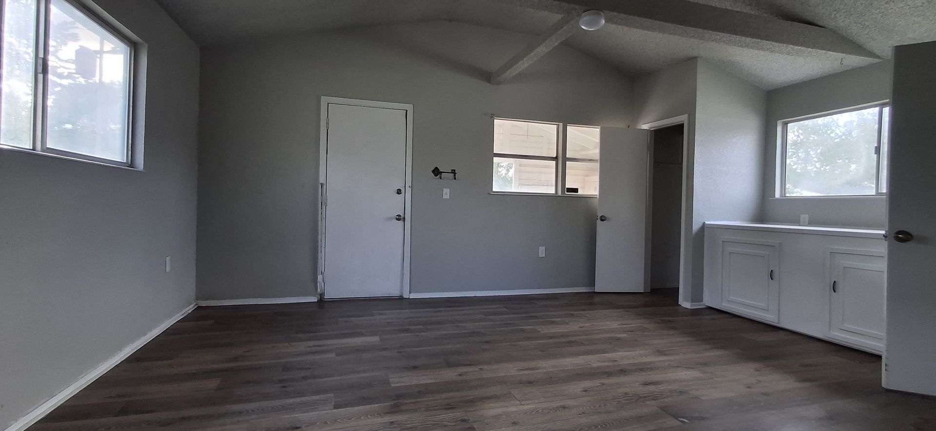 Empty room with gray walls and wood-look flooring; white doors and cabinets; a window on either side.