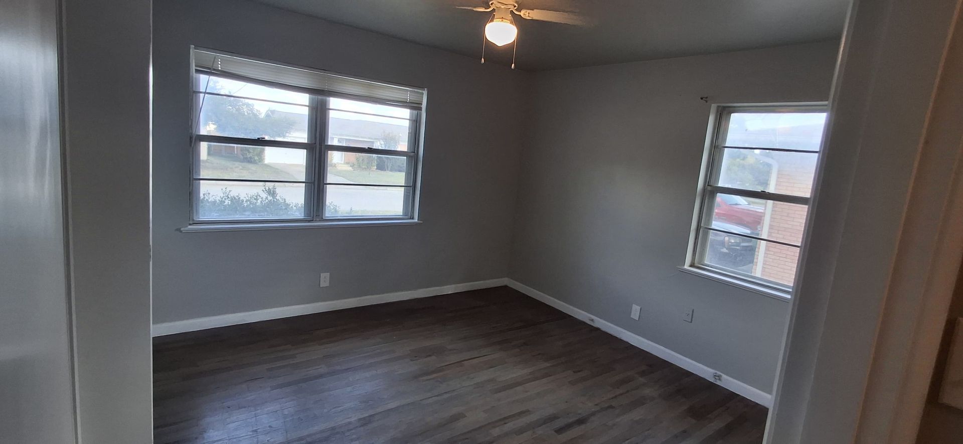 Empty room with two windows, gray walls, and wood-look flooring. A ceiling fan is visible.