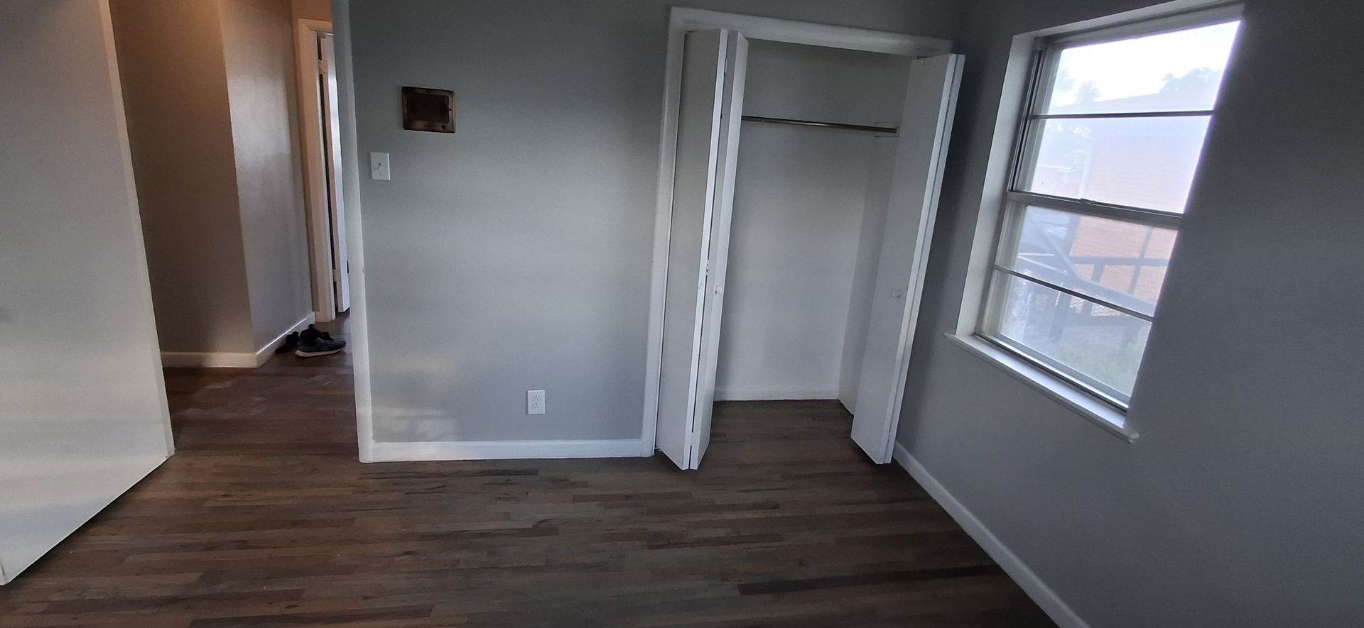 Empty room with a closet and a window. Wooden floor and gray walls.