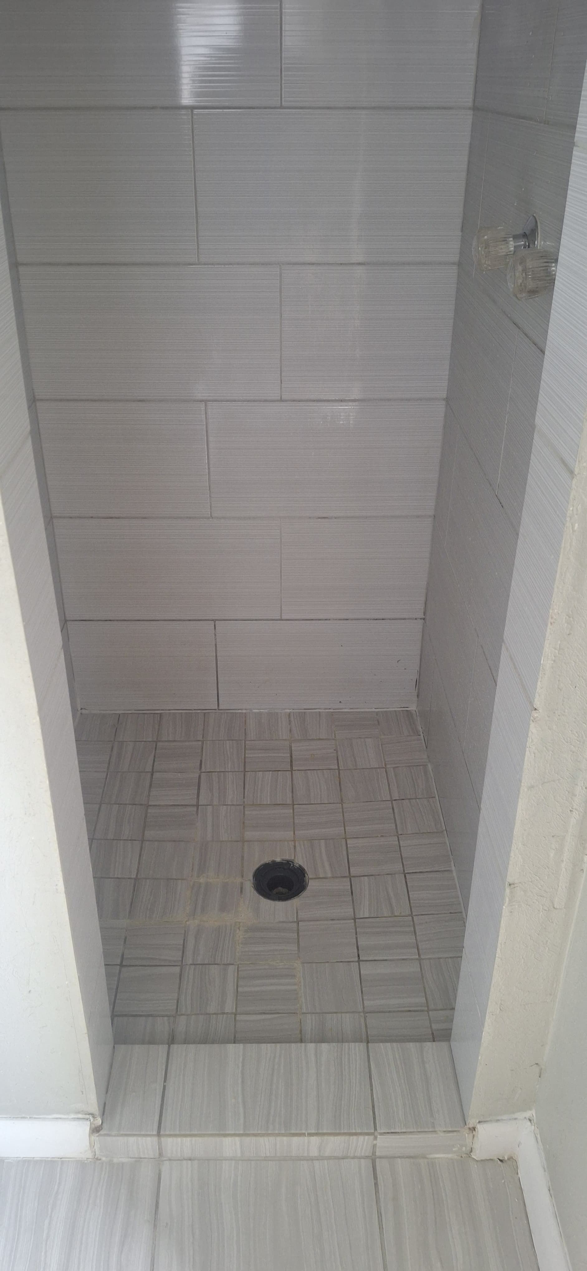 Grey tiled shower with drain in the center, lined by white walls.